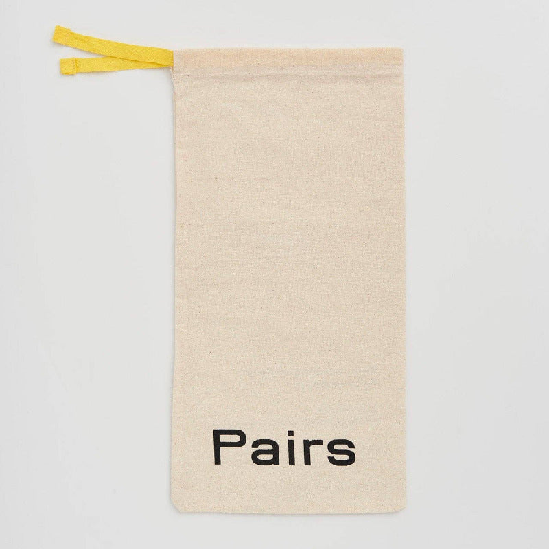 A beige canvas drawstring pouch with a bright yellow tie and the word 'Pairs' printed in black at the bottom, shown on a light gray background.