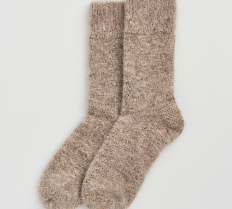 A pair of fuzzy, heathered knit socks in a warm taupe-beige color, displayed flat against a clean, light gray background.