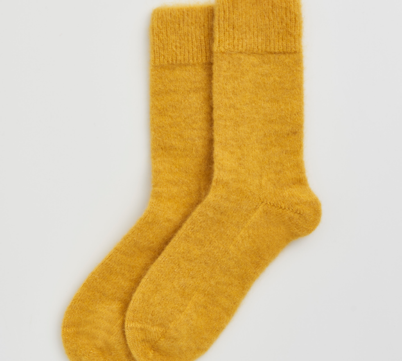 A pair of fuzzy, mohair-style mustard yellow socks shown flat against a light gray background.
