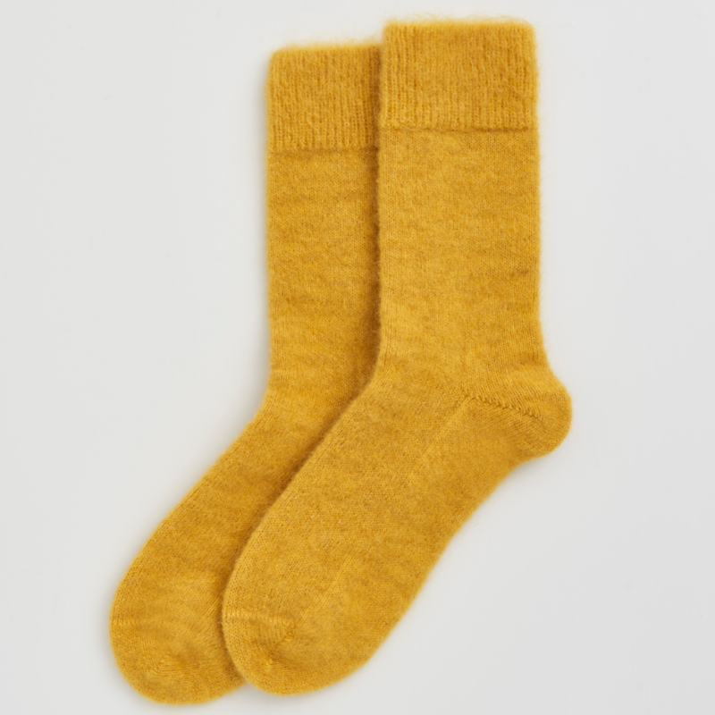A pair of fuzzy, mohair-style mustard yellow socks shown flat against a light gray background.