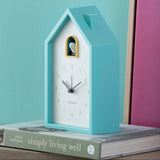 Blue cuckoo clock on a stack of books with a teal and pink background