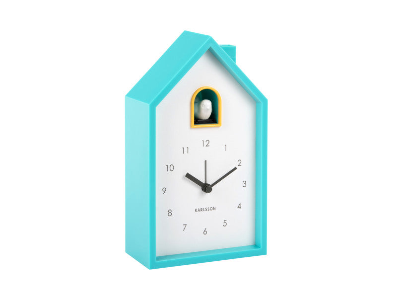 Turquoise clock shaped like a house with a white face on a white background