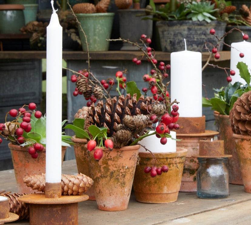 Decorative table setting with candles, terracotta potted plants, and festive elements on a wooden surface.