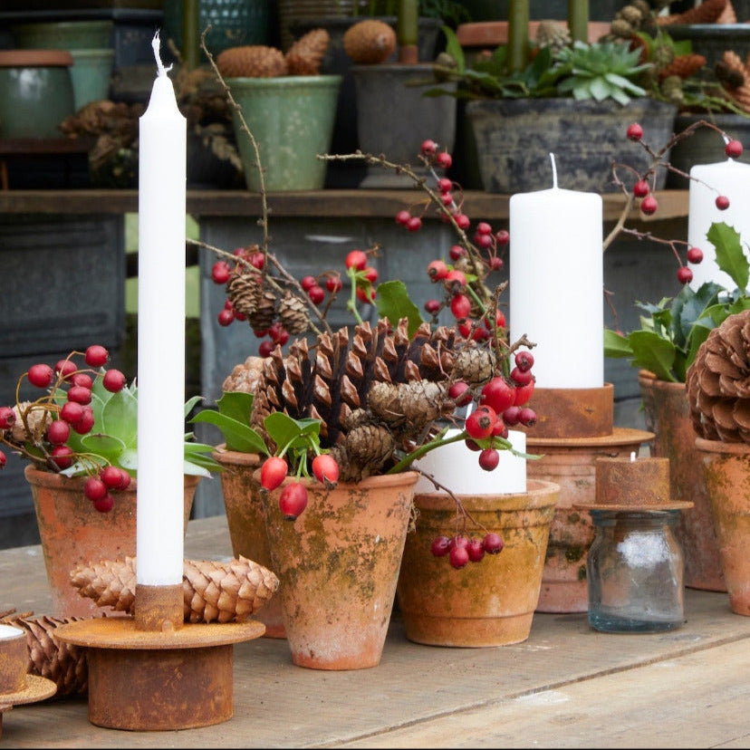 Decorative table setting with candles, terracotta potted plants, and festive elements on a wooden surface.