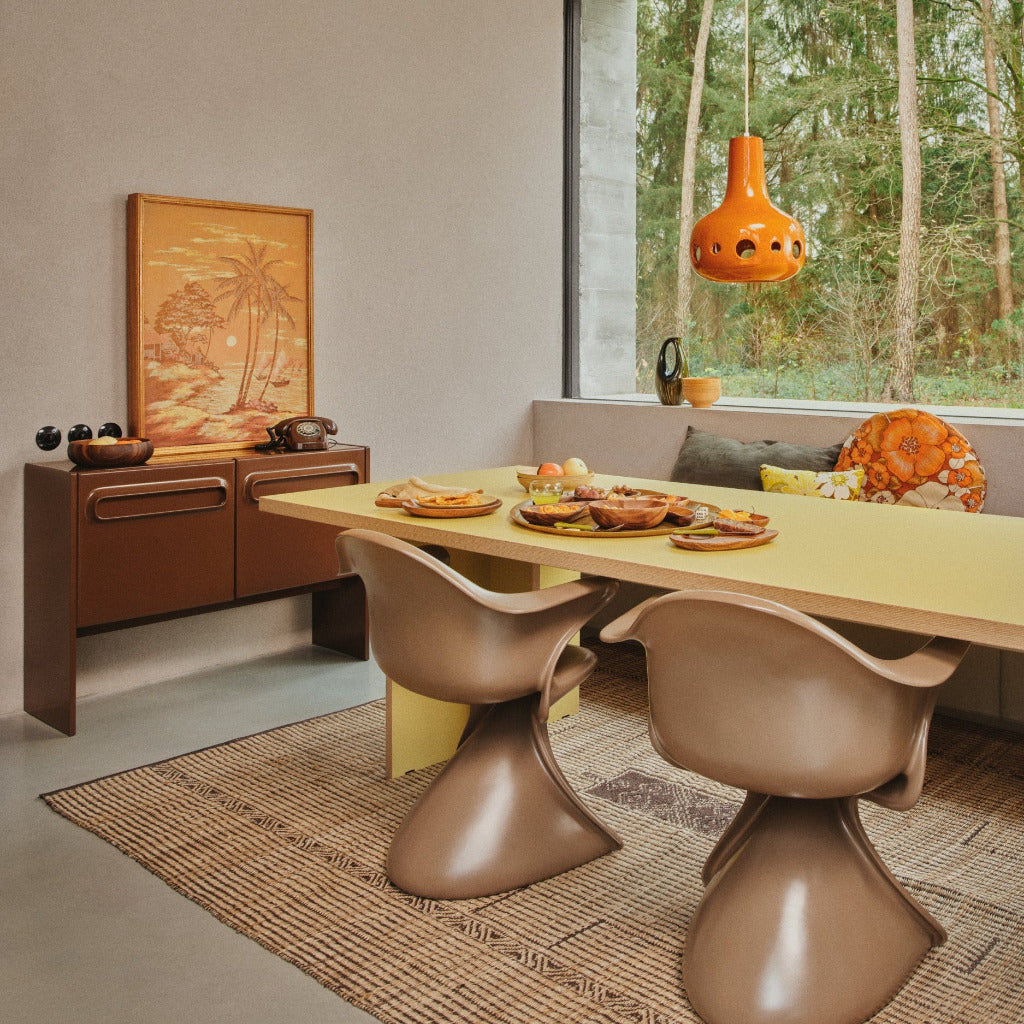Modern dining room with a yellow table and brown chairs, featuring a large window with a view of trees.