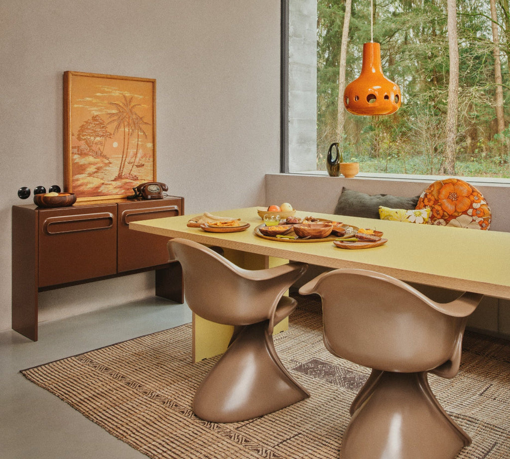 Modern dining room with a yellow table and brown chairs, featuring a large window with a view of trees.