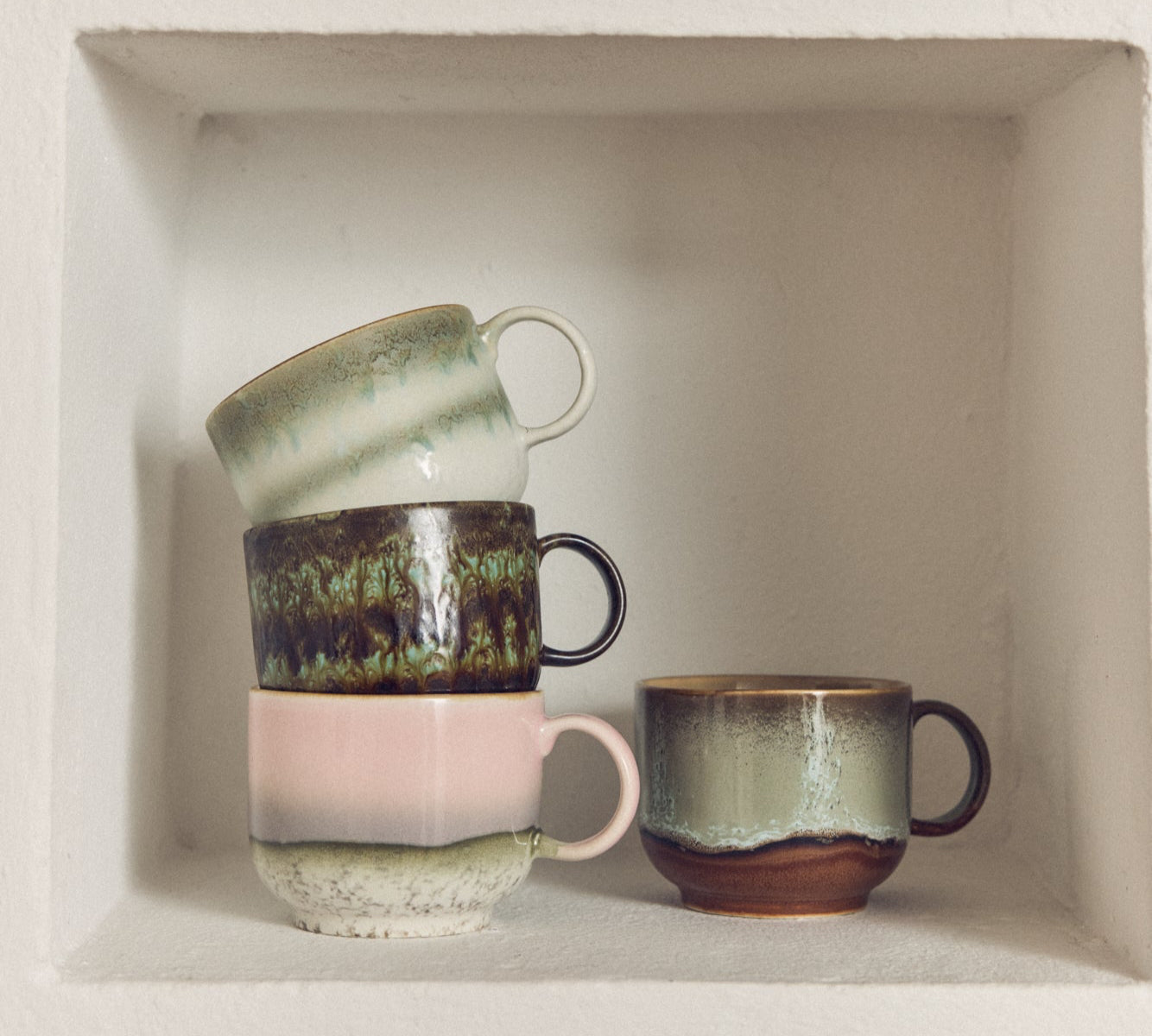 Set of ceramic mugs with different designs on a white shelf.