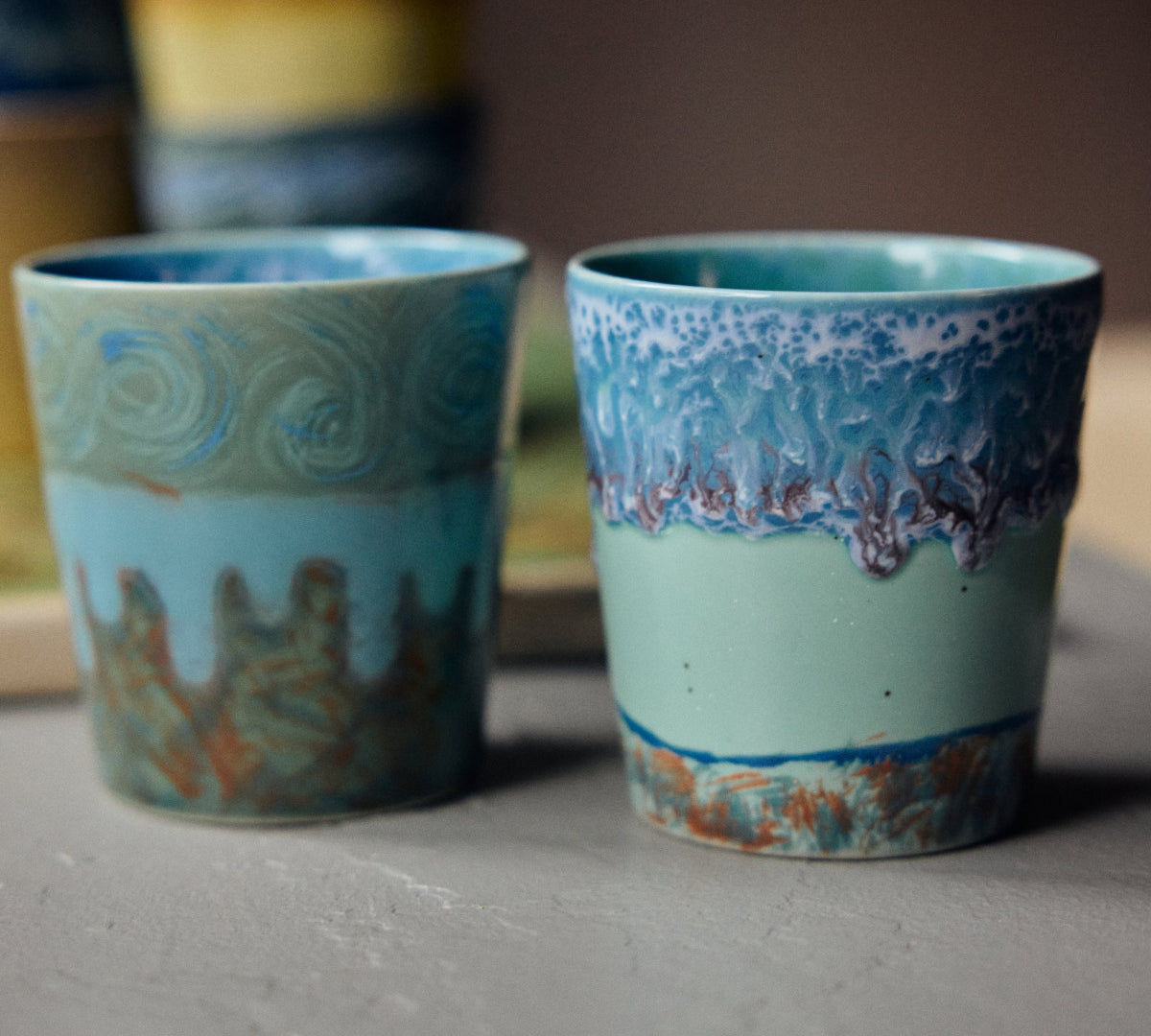 Two ceramic cups with decorative patterns on a wooden surface.