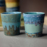 Two ceramic cups with decorative patterns on a wooden surface.