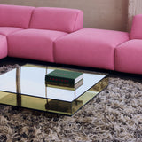 A bright pink modular sectional sofa in a loft-style room with an acrylic quare coffee table, a shag rug, and a window in the background.