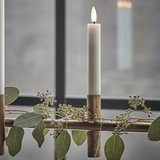 Two lit candles in wooden holders with greenery on a reflective surface.