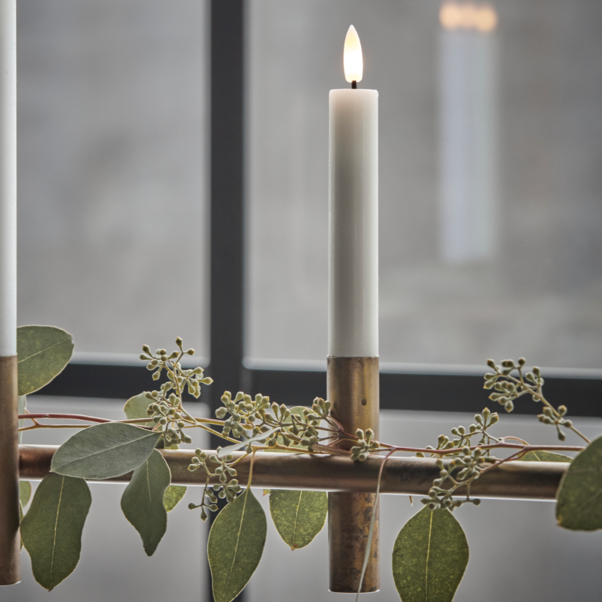 Two lit candles in wooden holders with greenery on a reflective surface.