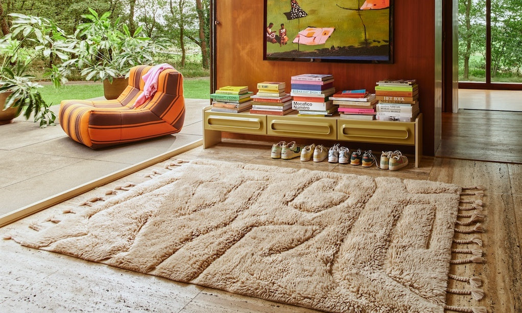 Living room with a large beige rug, colorful armchair, and bookshelf by HKLIVING