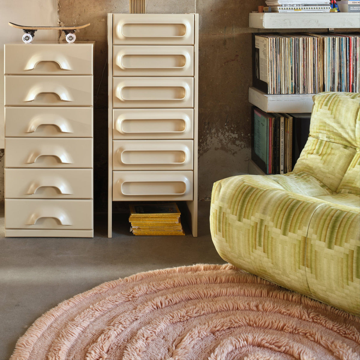 Modern interior with beige drawers, a yellow armchair, and a textured rug.
