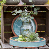 A styled arrangement of home decor items including two gray concrete planters, a glass mason jar filled with eucalyptus stems, a succulent, and greenery, displayed on a rustic wooden crate with a blue plate in the background.