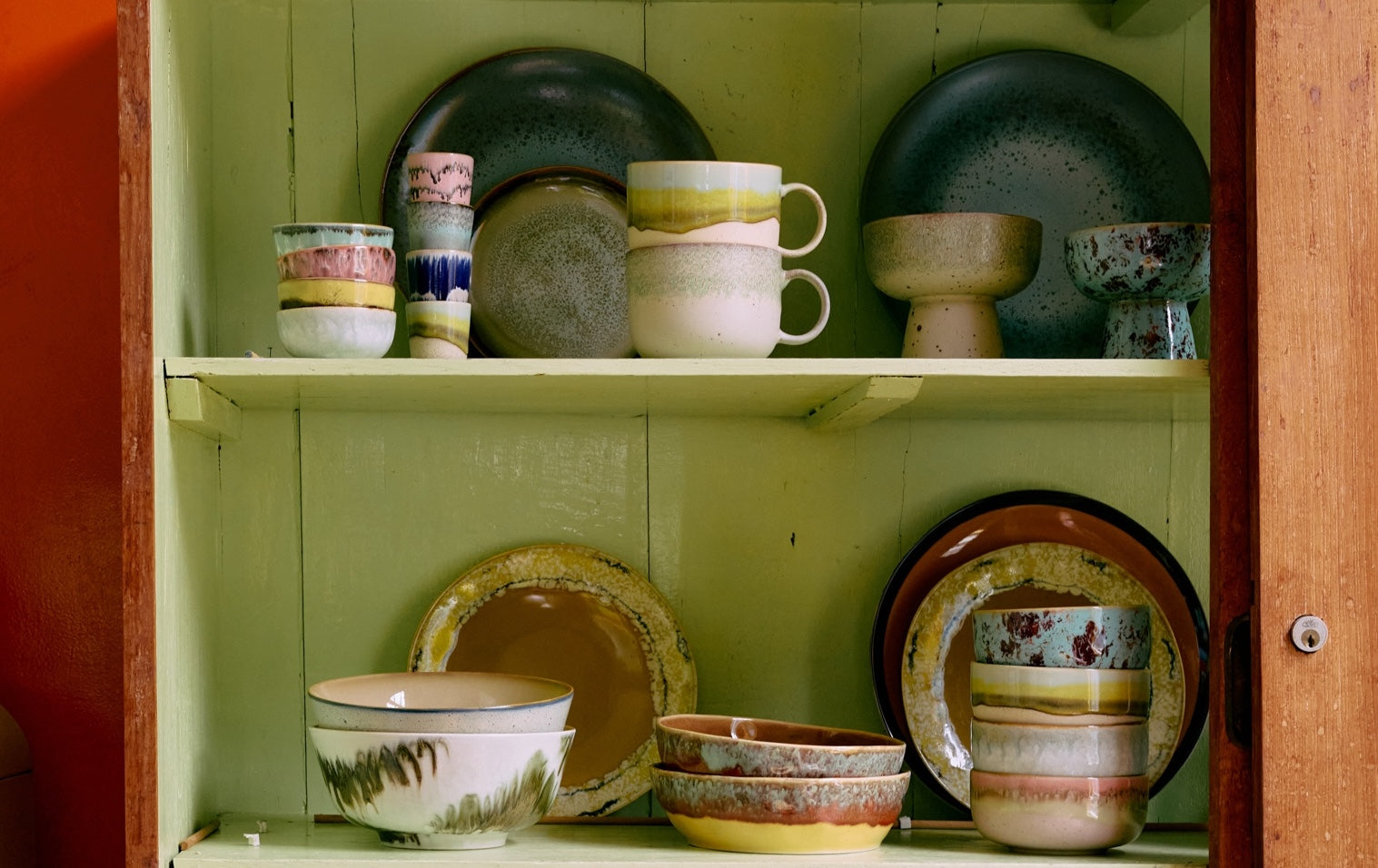 Collection of ceramic dishes on a shelf with a green wall background