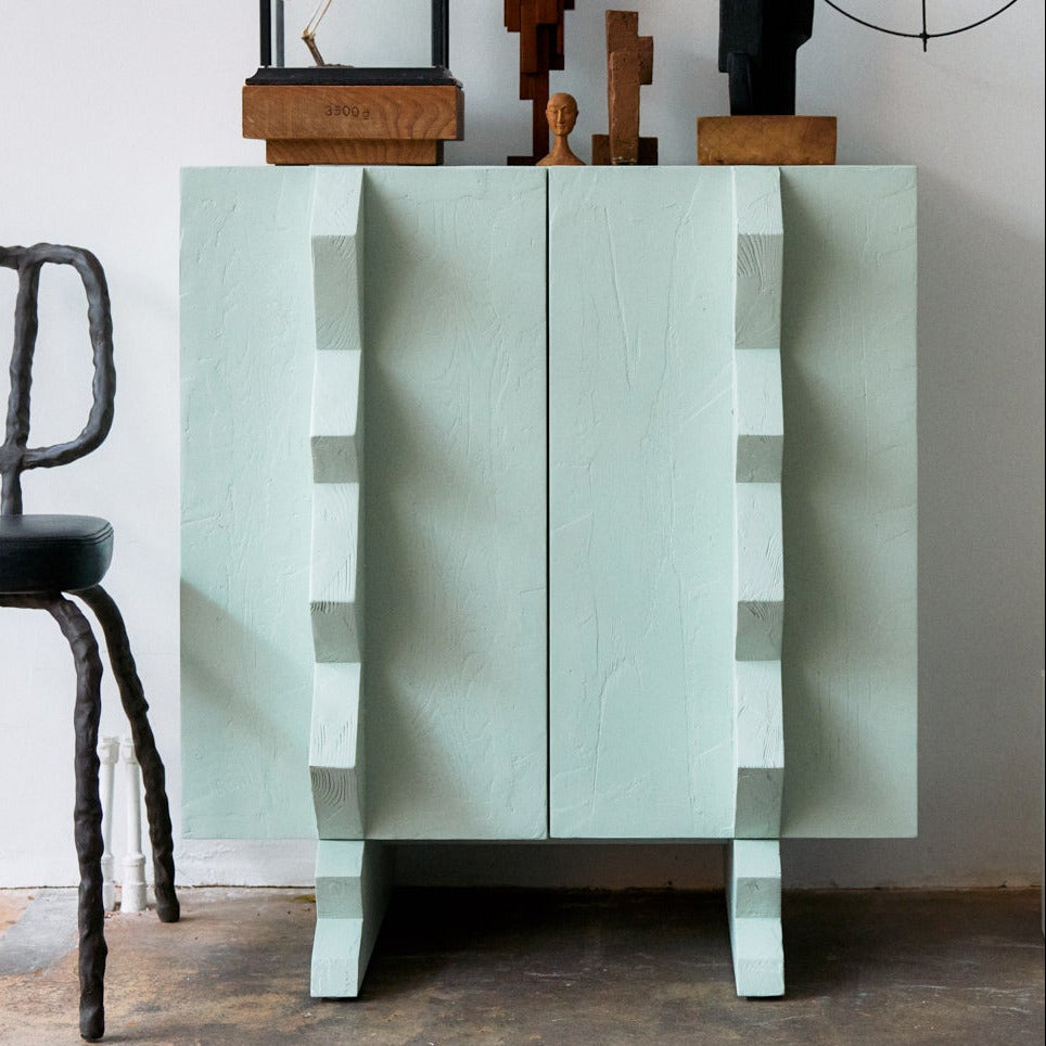 Modern interior with a light blue cabinet, black chair, and abstract sculpture.