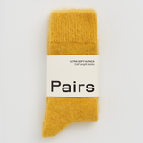 A pair of soft mustard yellow knit socks in their original packaging, featuring a white paper band with the brand name 'Pairs' printed in black.