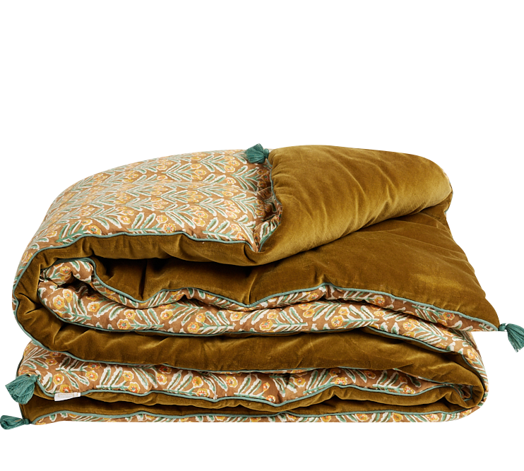 A folded quilted comforter with a rich mustard-gold velvet side and a patterned side featuring teal and orange botanical motifs, set against a plain white background.