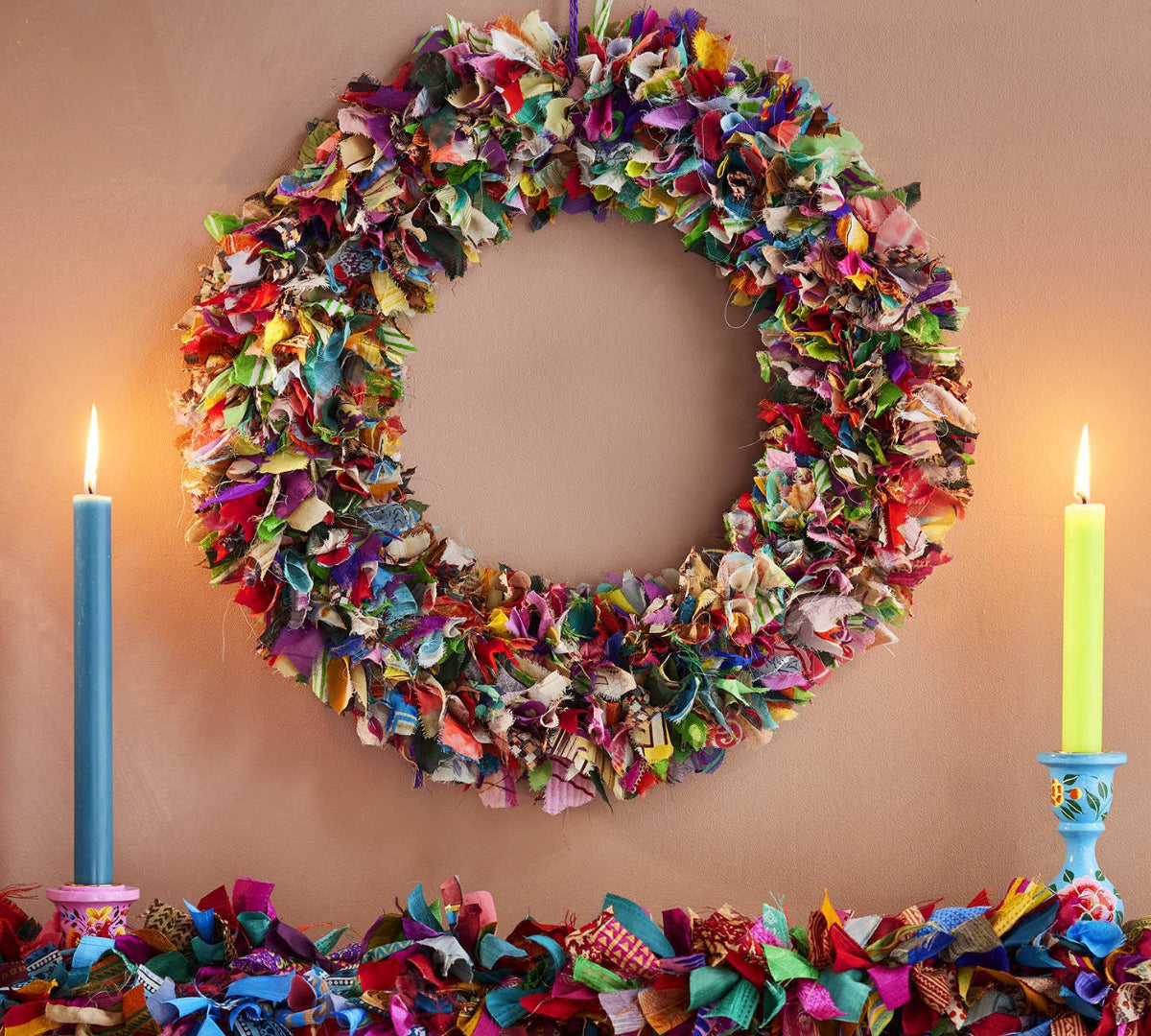 Colorful fabric wreath and garland on a wooden surface with candles.