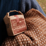 Person holding a small cardboard box of hot chocolate in a natural setting