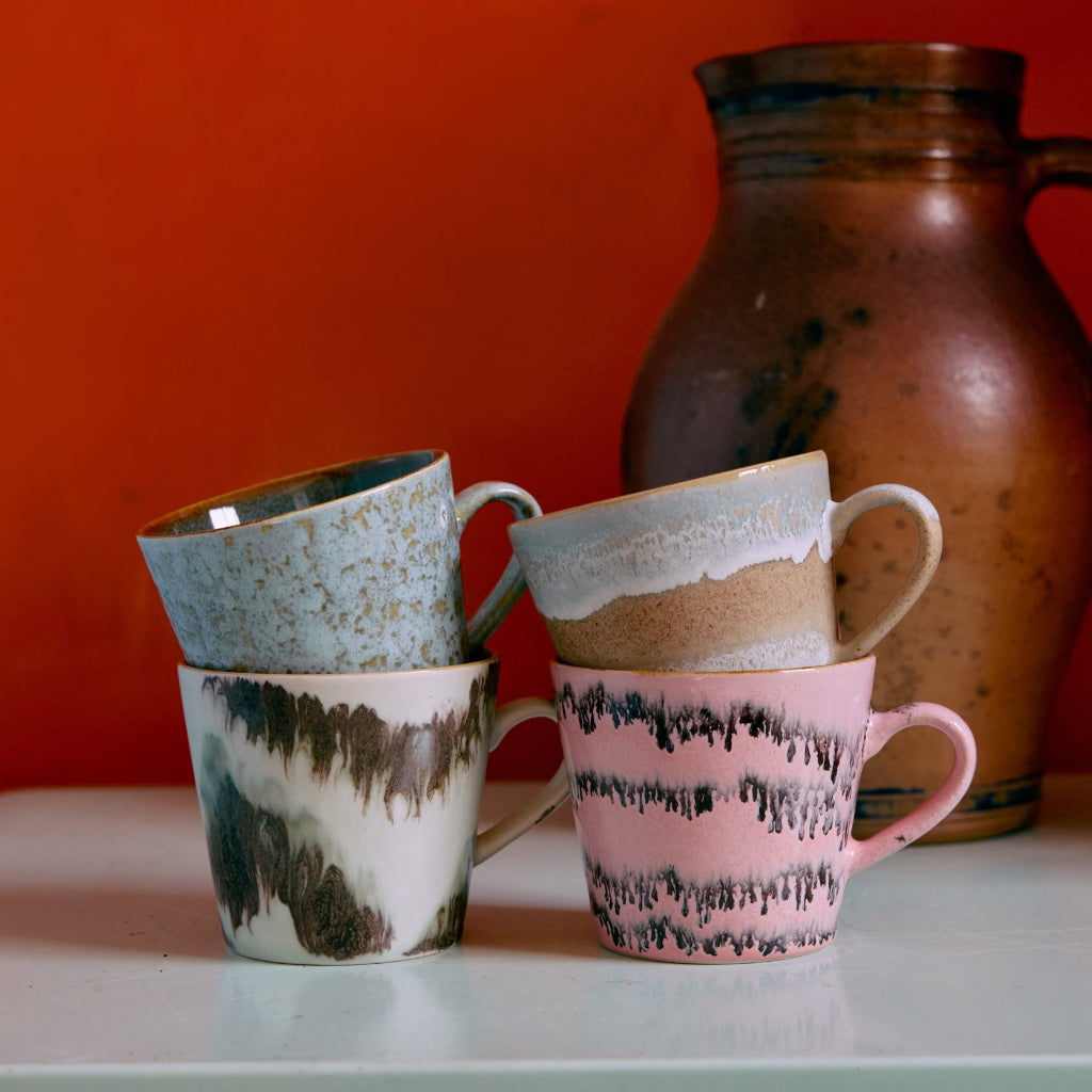 Four ceramic mugs with unique patterns on a white surface against an orange wall.