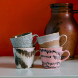Four ceramic mugs with unique patterns on a white surface against an orange wall.