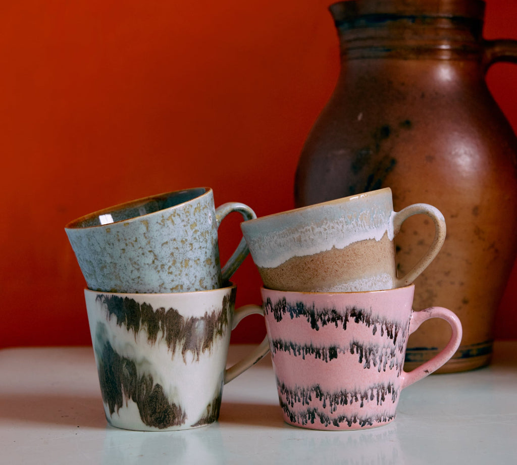 Four ceramic mugs with unique patterns on a white surface against an orange wall.