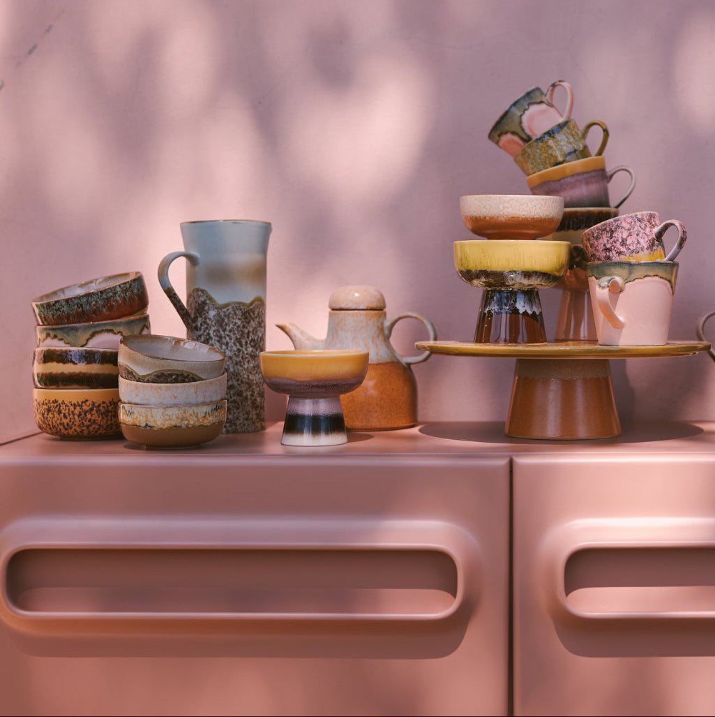 Collection of ceramic teapots and cups on a CABINET with a pink background