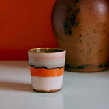 Ceramic cup with multicolored stripes on a white surface with a red background