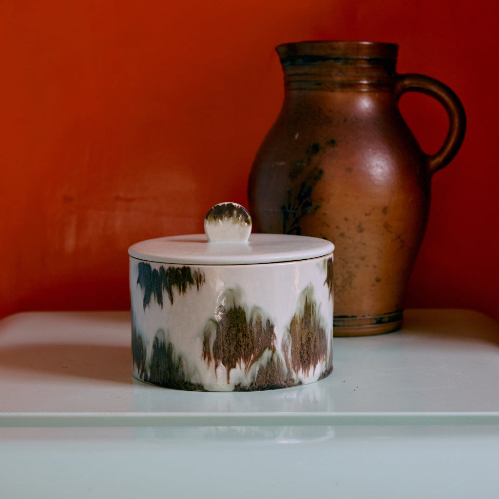 Ceramic container with a lid and a pitcher against an orange wall.