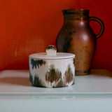 Ceramic container with a lid and a pitcher against an orange wall.