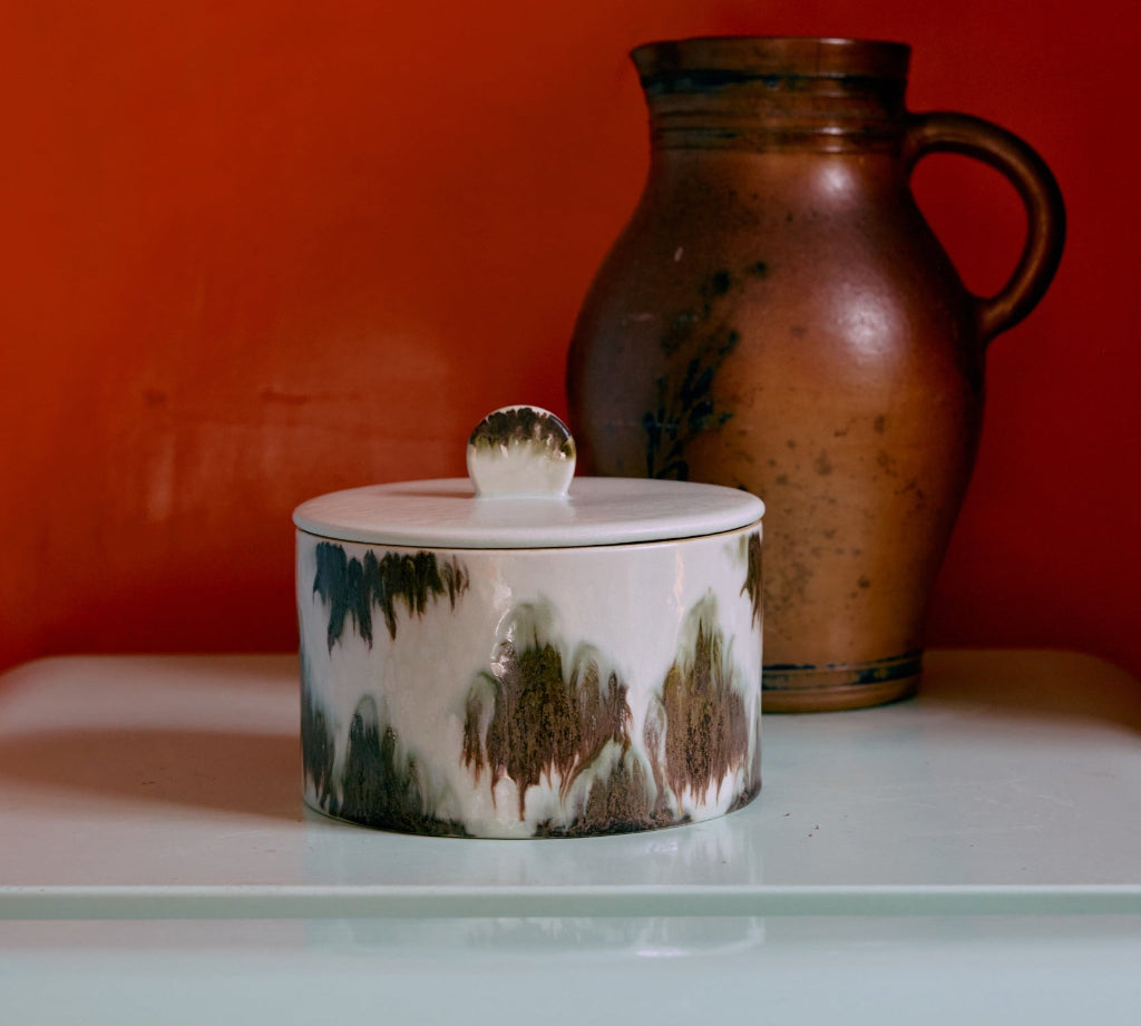 Ceramic container with a lid and a pitcher against an orange wall.