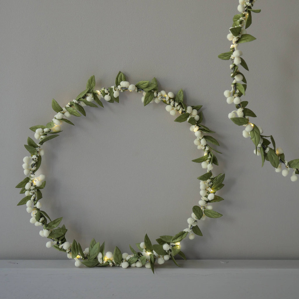 Decorative wreath with green leaves and white berries on a gray background