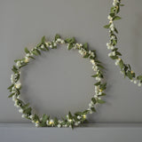 Decorative wreath with green leaves and white berries on a gray background