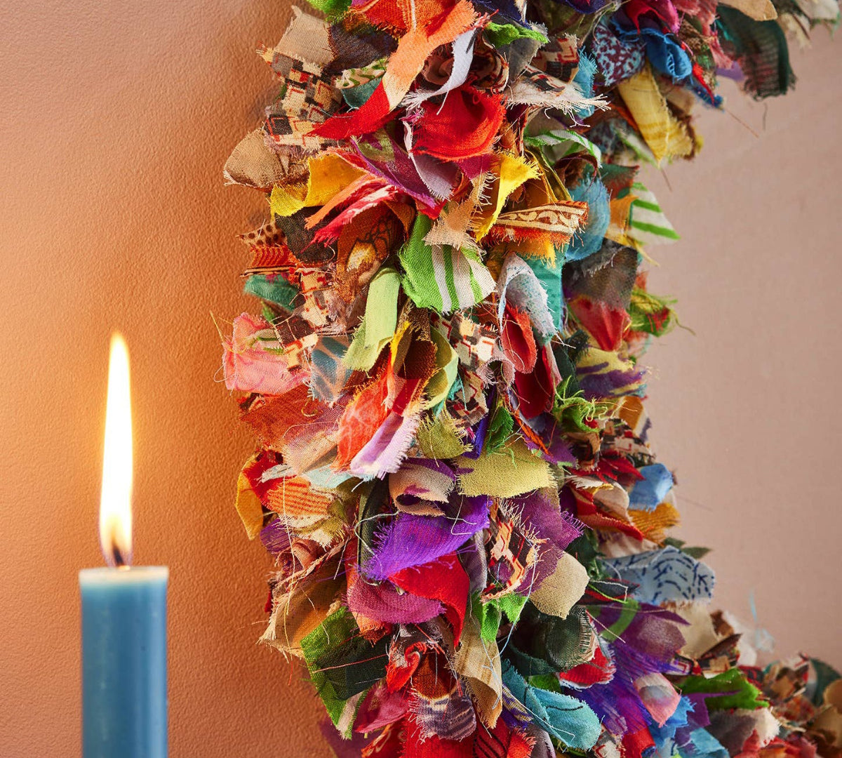 Colorful fabric wreath with a lit candle on a plain background