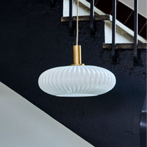 Modern white pendant light hanging in a staircase with black railing and white steps.
