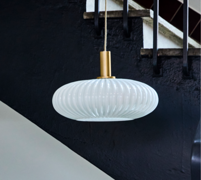 Modern white pendant light hanging in a staircase with black railing and white steps.