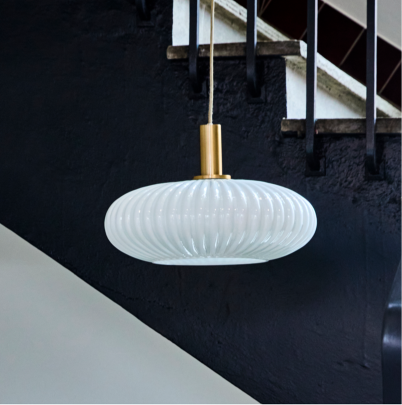 Modern white pendant light hanging in a staircase with black railing and white steps.