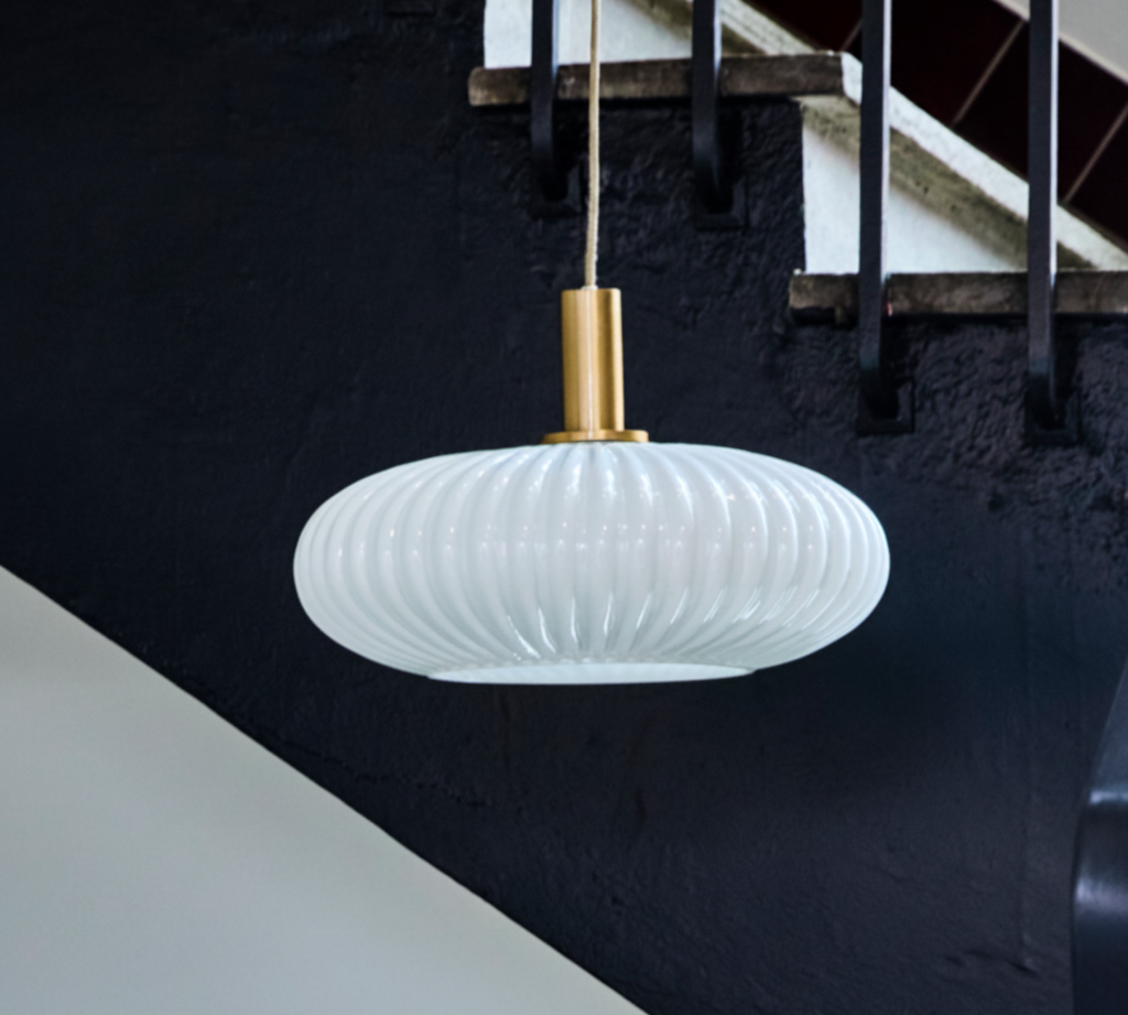 Modern white pendant light hanging in a staircase with black railing and white steps.