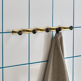 brass towel rack with black hooks on a tiled wall with blue grout.