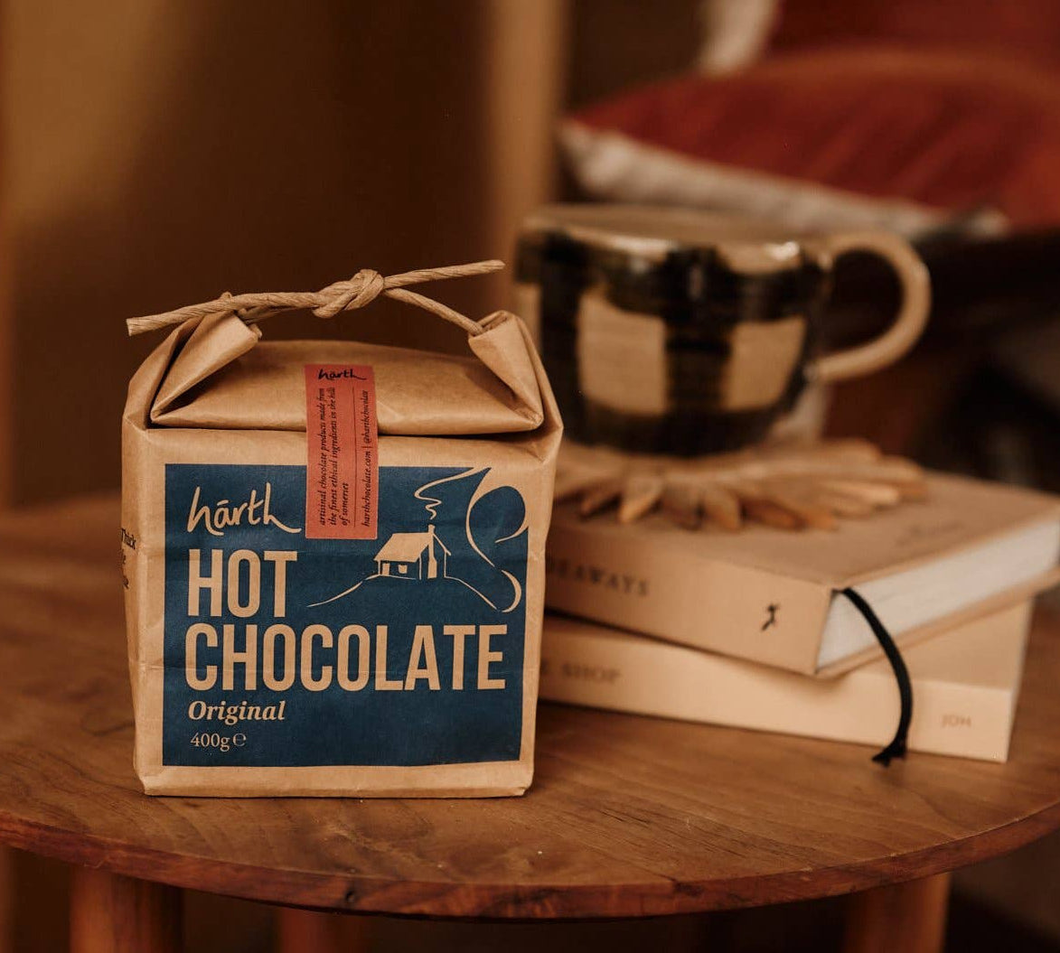 Box of hot chocolate on a wooden table with books and a mug in the background