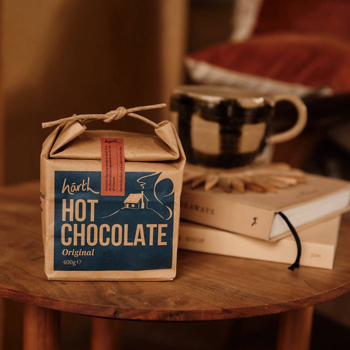 Box of hot chocolate on a wooden table with books and a mug in the background