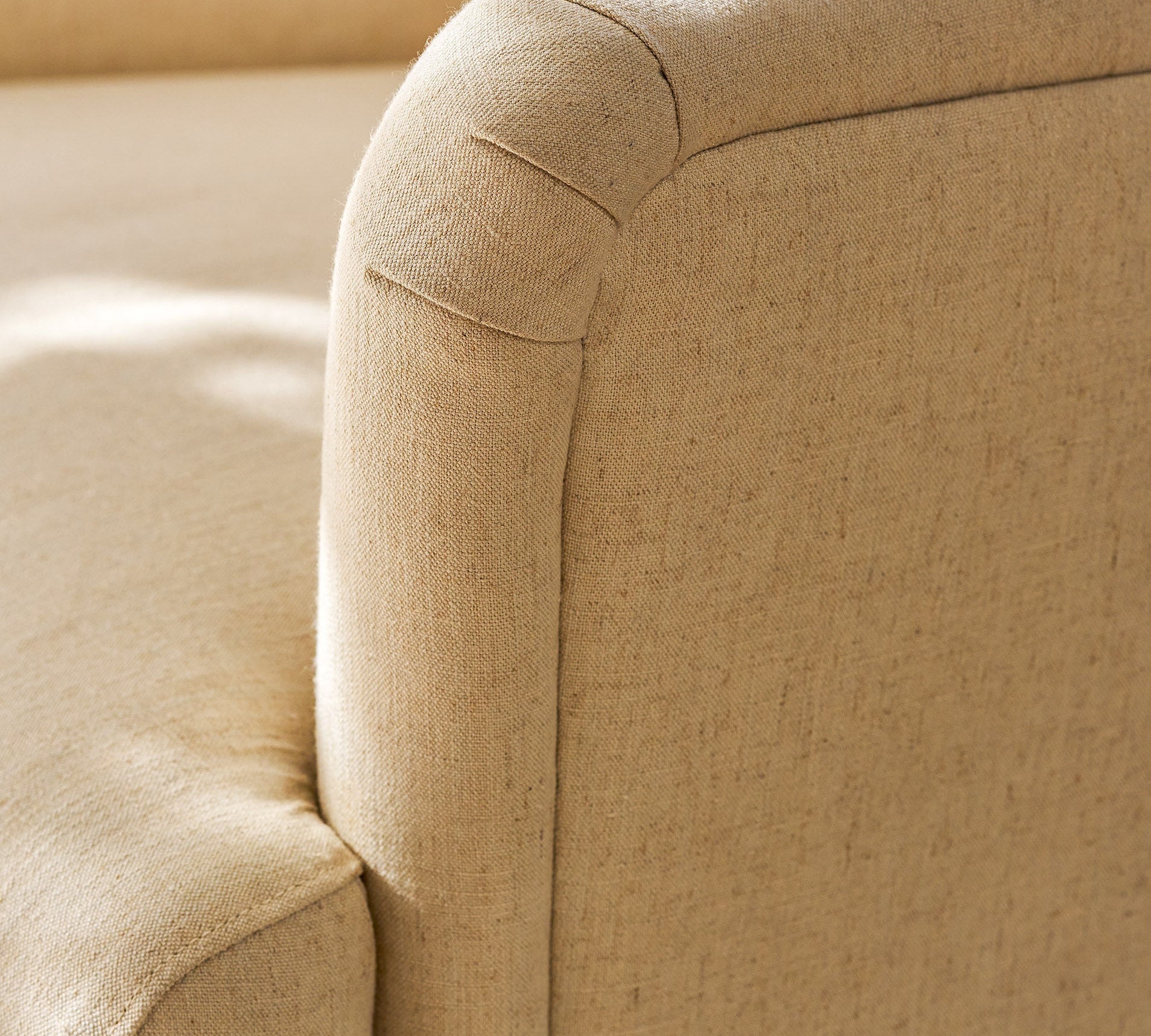 Close-up of a beige upholstered armchair showing the fabric texture and rounded arm detail in warm natural light.