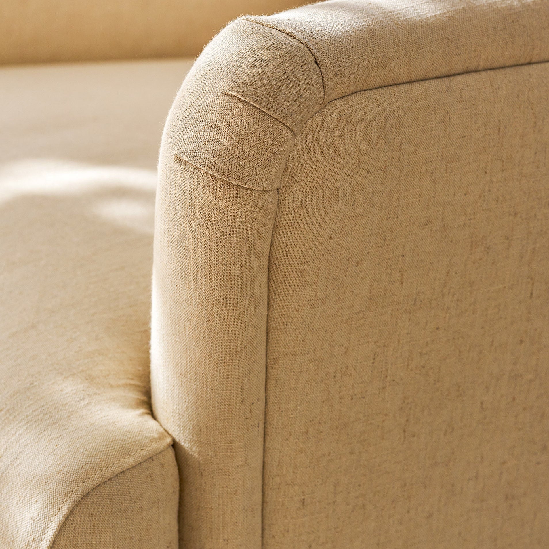 Close-up of a beige upholstered armchair showing the fabric texture and rounded arm detail in warm natural light.