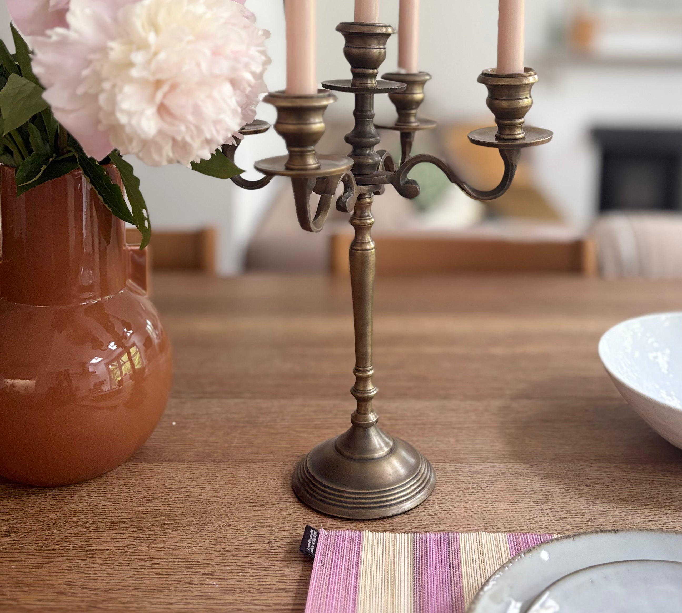 Bronze candelabra with lit candles on a wooden table, next to a vase with flowers and a bowl.