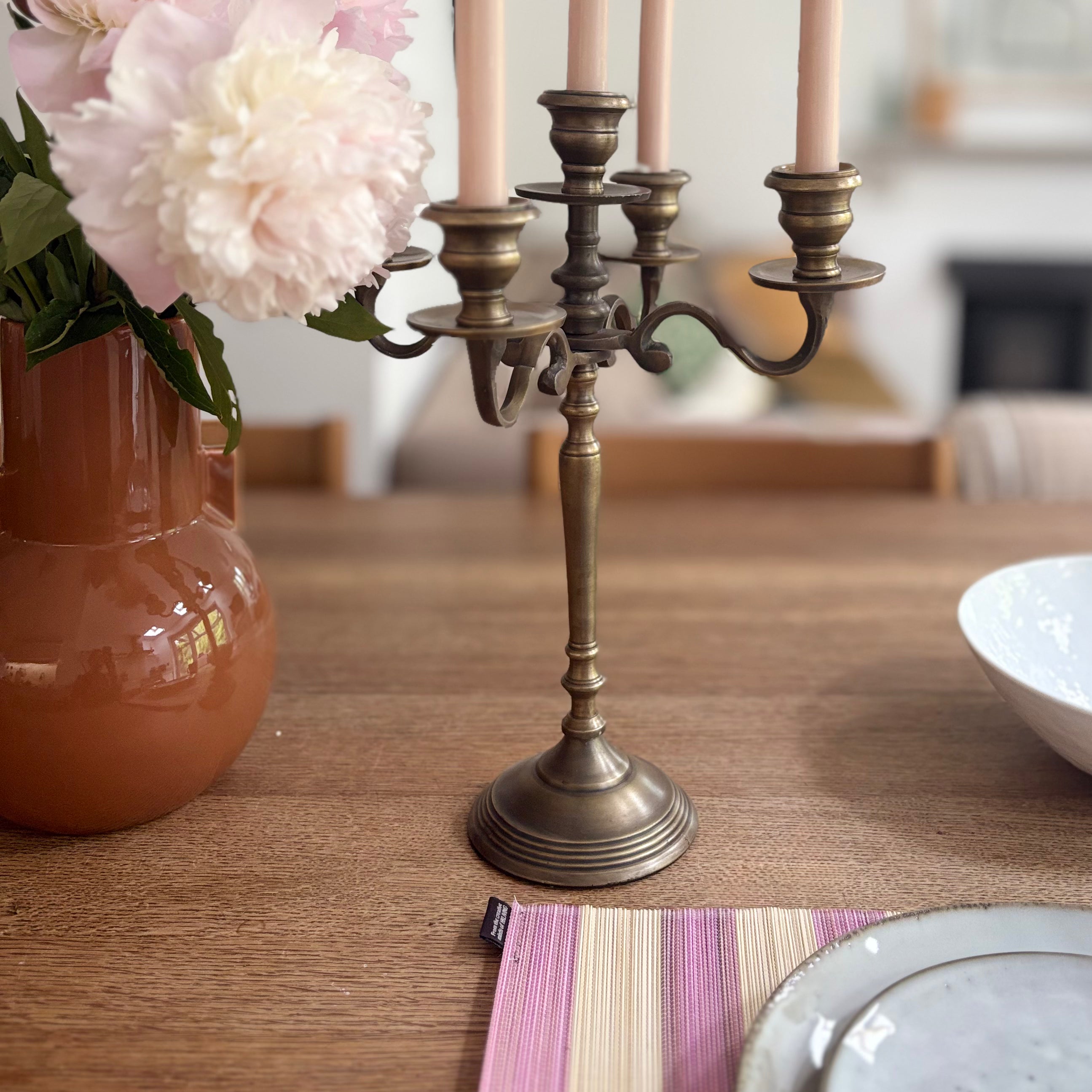 Bronze candelabra with lit candles on a wooden table, next to a vase with flowers and a bowl.