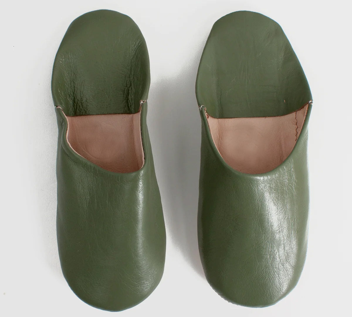 A pair of olive green leather slip-on slippers with a contrasting tan interior lining, photographed from a top-down angle on a light gray background.
