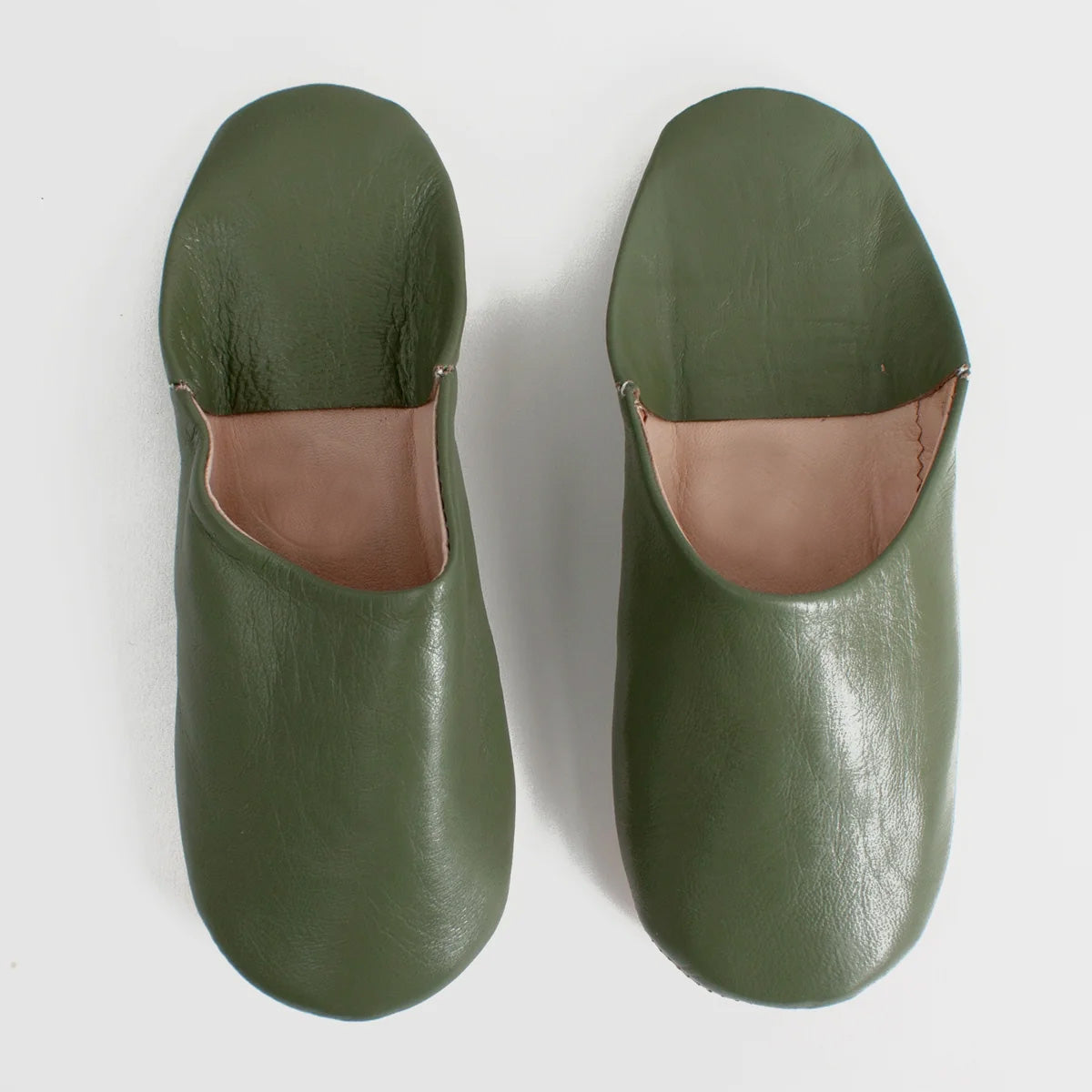 A pair of olive green leather slip-on slippers with a contrasting tan interior lining, photographed from a top-down angle on a light gray background.