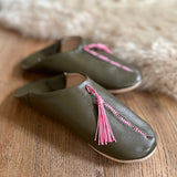 Pair of green leather slippers with pink tassels on a wooden surface.